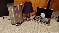 Photo showing stainless steel trashcan, New England Patriots lamp, and poker chip set in metal case on carpeted floor with wood panel wall background.