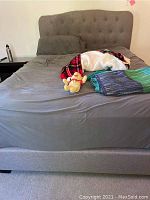 Front view of the fully assembled gray upholstered queen bed with tufted headboard showing bedding and a plush toy on the bed.