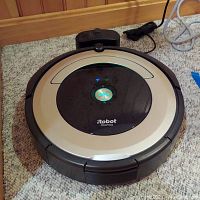 Top view of iRobot Roomba 690 robot vacuum on carpet with charging base behind it.