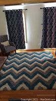 Full view of the chevron patterned shag rug laid on wooden floor in front of a window with curtains and a chair nearby