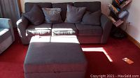 Gray fabric Bauhaus style three-seat sofa with six matching accent pillows on a red carpet.
