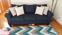 Front view of navy blue sofa with four accent pillows on patterned rug