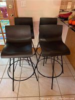 Four black plastic swivel bar stools grouped together on tile floor showing seat shape and metal legs.