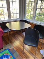 Overall view of black square table and four matching chairs in corner room with wood floor.