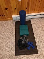 View of all items showing foam roller, foam blocks, exercise mat and various dumbbells placed on the mat on carpeted floor.