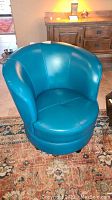 Front view of one teal swivel barrel chair on area rug showing seat cushion, curved back and stitching detail