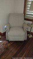 Front view of the beige fabric Bassett armchair with nailhead trim and padded back