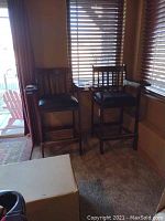 Two bar-height billiard chairs side by side in front of window