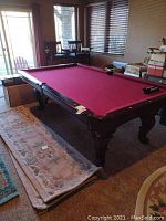 Full side view of the dark wood billiard table with red felt in room setting