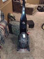 Front view of the Bissell carpet cleaner standing upright on carpet with couch and furniture in background.