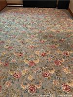 Full view of large rectangular carpet showing overall floral pattern with red, yellow, pink, blue flowers and green leaves on light blue-gray background.
