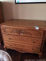 Front view of the wooden chest showing three drawers and carved detail on the top drawer panel and bottom skirt.
