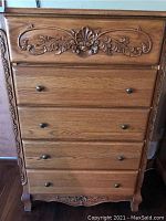 Front view of five drawer chest showing carved top drawer and metal knobs