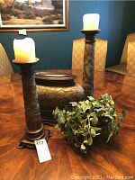Photo showing all four pieces arranged on a wooden dining table: two matching candlesticks with white candles, one different candlestick, a rectangular lidded metal container, and an artificial ivy plant.