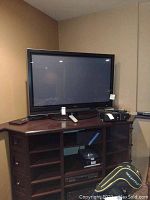 Full view of the Hitachi 50-inch flat screen TV sitting on a wooden media console with remote and other small electronics nearby.