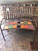 Front view of handcrafted rustic iron bench showing colorful ceramic tile seat and decorative iron backrest with diamond accents.