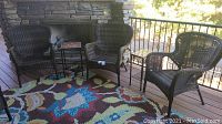 Three brown wicker chairs arranged on wood deck with patterned rug and small side table.