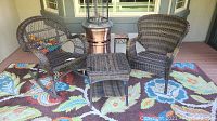 Set of three modern outdoor wicker pieces: rocker chair, stationary chair, and side table on a floral patio rug.