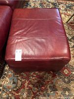 Top view of reddish-brown leather ottoman showing smooth leather surface and stitched detailing.