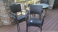 Four matching dark brown woven wicker/rattan outdoor armchairs with metal frames shown stacked and arranged on wooden deck patio.