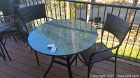 Round outdoor table with clear glass top on a metal frame, on wooden deck