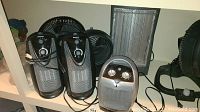Photo showing four space heaters and two black tabletop fans arranged on a shelf.