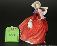Front angle view of the Royal Doulton figurine showing the flowing red dress and bonnet hat with white and purple details.