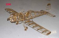 Decorative brass airplane sculpture with detailed open-framework design, visible cockpit, propeller, and landing gear, shown from front left angle.