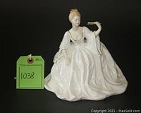 Front view of the white porcelain figurine of a seated lady in ball gown with fan.