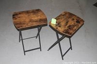 Two folding TV table stands side by side, showing rustic wood finish tops and black metal folding frames.