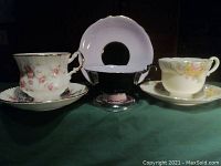 Front view of three tea cups and matching saucers showing floral and solid lavender designs with gold trim, no chips or cracks visible