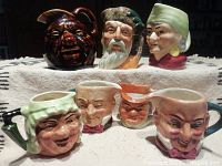 Seven miniature Toby jugs displayed on a cloth surface showing detailed character faces and hats.