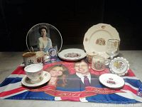 Wide view showing all royalty memorabilia items including cups, mugs, plates, glassware and cloth with royal portraits.
