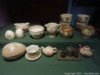 Assorted small china pieces laid out on a table including cups, teapots, jugs, bowls, and decorative egg-shaped container.