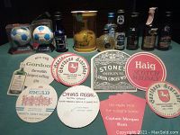 Photo showing two St Andrews 1998 France World Cup collectible soccer ball miniatures in display boxes, three miniature liquor bottles (including Premier Canadian Club, Harveys Bristol Cream, Baileys Irish Cream), and several round and oval vintage bar coasters.