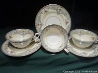 Three Royal Worcester tea cups paired with their matching saucers, showing cream and white porcelain with blue and gold trim and raised floral detailing.