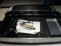 View with removable ridged grill plate inverted over appliance base showing included power cord and user manual inside appliance tray