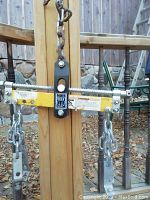 Close-up photo of the engine hoist leveler showing Power Fist logo, metal chains, adjustable notched bar and warning label.