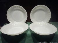 Four white milk glass bowls with swirl design placed together, showing front view with round shape and raised swirl edges.