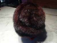 Brown fur winter hat shown from exterior top and side angles, showcasing plush fur texture and round shape.
