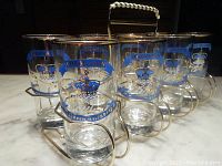 Front angle showing 8 glasses with blue and gold coronation design in metal rack with handle.
