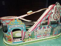 Front and side view showing colorful carnival-themed tin wind-up roller coaster with track and coaster car in place.