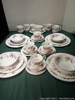Full set of place settings arranged on table including plates, bowls, cups, saucers, mugs, and gravy boat.