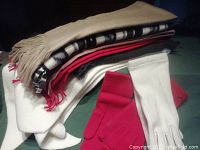 Stack of folded scarves showing various colors including cream, black and white checkered, red, gray, and white, with red and white gloves placed in front.