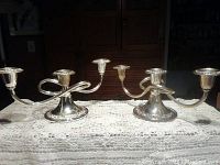 Pair of silver plated candelabras on a lace tablecloth, showing the curved arms, three candle holders each, and round bases with decorative edges.