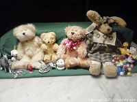 Full lot overview showing three stuffed bears, one stuffed dog in plaid dress, and assortment of small toys including marbles and figurines.