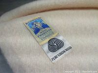 Close-up of Kenwood label on cream wool blanket indicating pure virgin wool and wool products famous brand.
