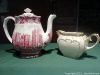 Photo showing Lambeth Palace coffee pot with red transferware print and Sadler iridescent creamer with gold trim on green surface.