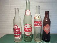 Front view of four vintage glass pop bottles Kist, Dr Pepper, Coca-Cola, and Orange Crush.