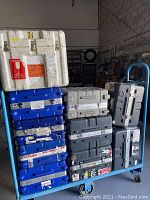 10 large industrial protective cases stacked on a dolly. Mix of white, gray, and blue cases with latches and reinforced corners visible.